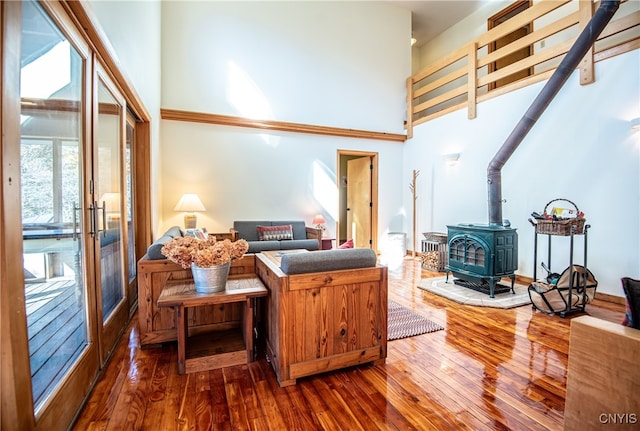 living room featuring a towering ceiling, a wood stove, and wood-type flooring