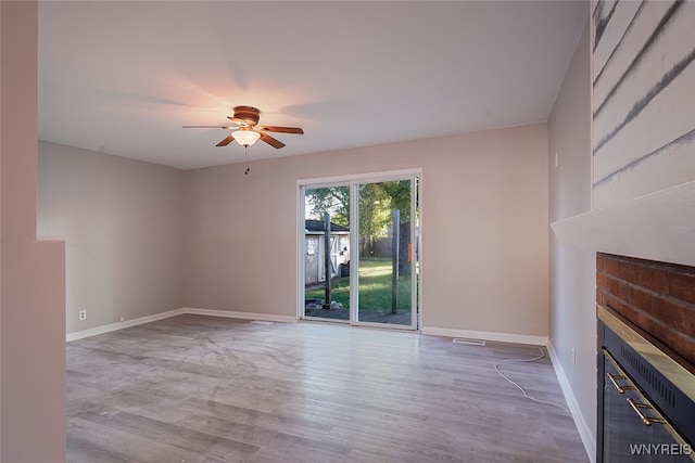 unfurnished living room featuring a brick fireplace, hardwood / wood-style flooring, and ceiling fan