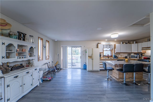 kitchen with hardwood / wood-style floors, white cabinetry, white refrigerator with ice dispenser, and a breakfast bar area