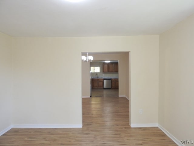 unfurnished room featuring an inviting chandelier, sink, and light wood-type flooring