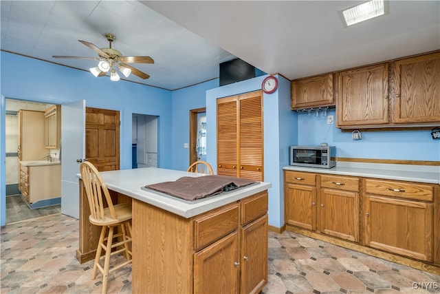 kitchen featuring a kitchen island, stainless steel cooktop, sink, a breakfast bar, and ceiling fan