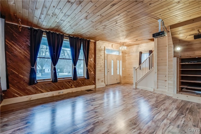 unfurnished living room featuring wooden walls, hardwood / wood-style flooring, a chandelier, and wooden ceiling