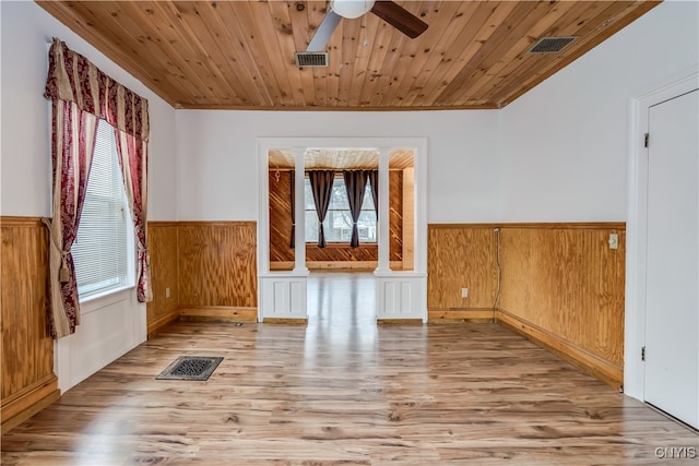 empty room featuring light hardwood / wood-style floors, decorative columns, a wealth of natural light, and wood ceiling