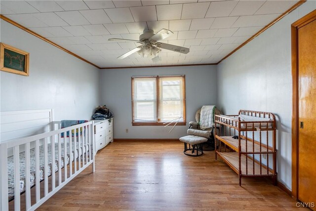 bedroom with crown molding, a crib, a ceiling fan, baseboards, and wood finished floors