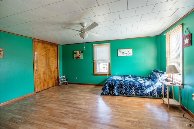 bedroom featuring baseboards, ceiling fan, multiple windows, and wood finished floors