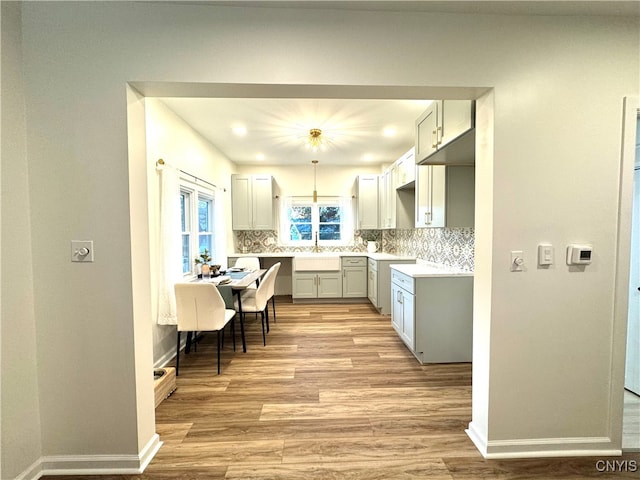 kitchen with sink, decorative backsplash, decorative light fixtures, and light wood-type flooring