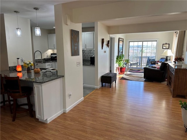 interior space with a kitchen breakfast bar, dark stone counters, hardwood / wood-style flooring, white cabinets, and hanging light fixtures