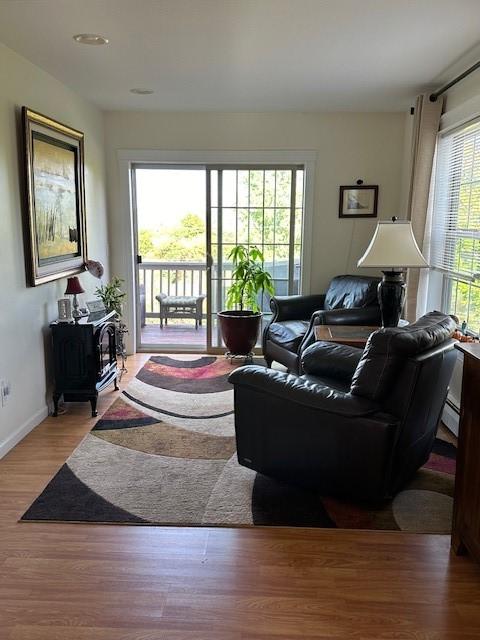 living room featuring wood-type flooring, a wood stove, and a baseboard heating unit