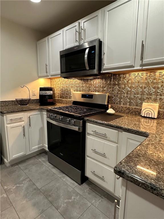 kitchen with backsplash, white cabinetry, stainless steel appliances, and dark stone counters