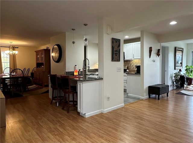 kitchen with a kitchen bar, wood-type flooring, decorative light fixtures, and white cabinetry