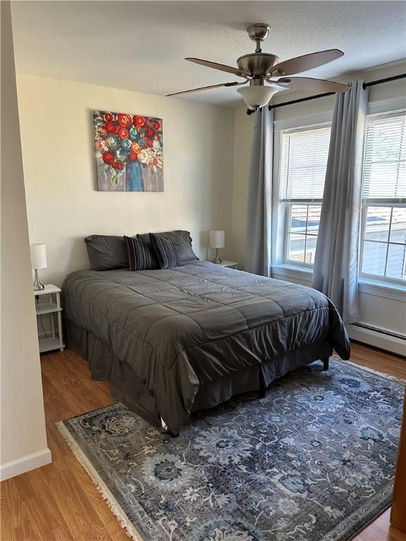 bedroom featuring hardwood / wood-style floors, a baseboard radiator, and ceiling fan