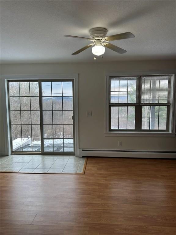 unfurnished room with a baseboard heating unit, light hardwood / wood-style floors, ceiling fan, and a healthy amount of sunlight