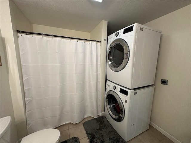 laundry room with light tile patterned floors, a textured ceiling, and stacked washing maching and dryer