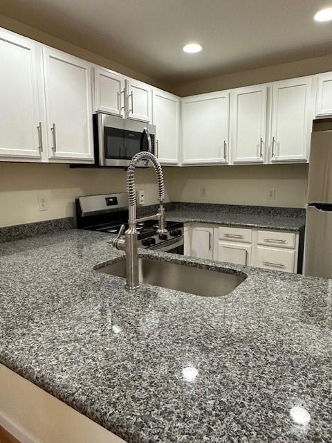 kitchen with white cabinets, appliances with stainless steel finishes, and dark stone counters