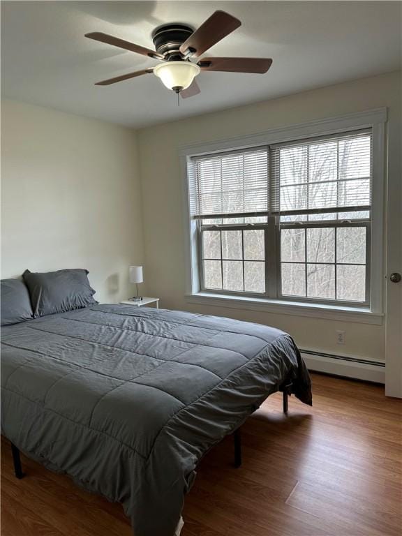 bedroom featuring hardwood / wood-style floors, baseboard heating, and ceiling fan