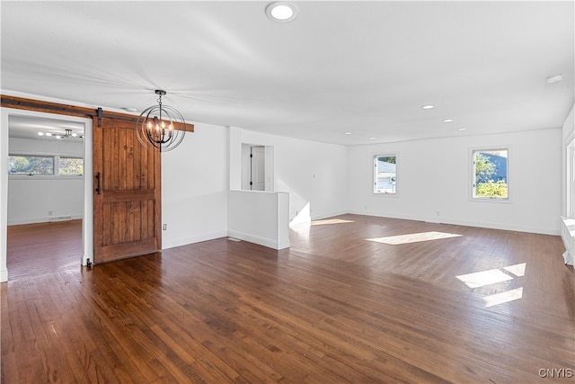 unfurnished living room with a chandelier, a barn door, and dark hardwood / wood-style floors