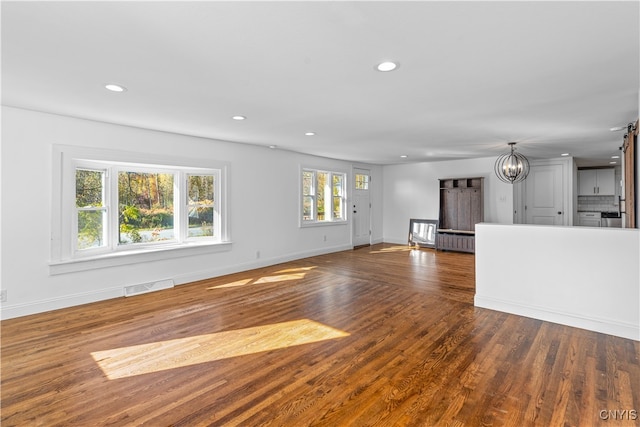 unfurnished living room with a notable chandelier, plenty of natural light, and dark hardwood / wood-style flooring