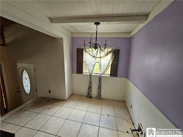 unfurnished dining area with a notable chandelier, beam ceiling, wooden walls, and light tile patterned floors