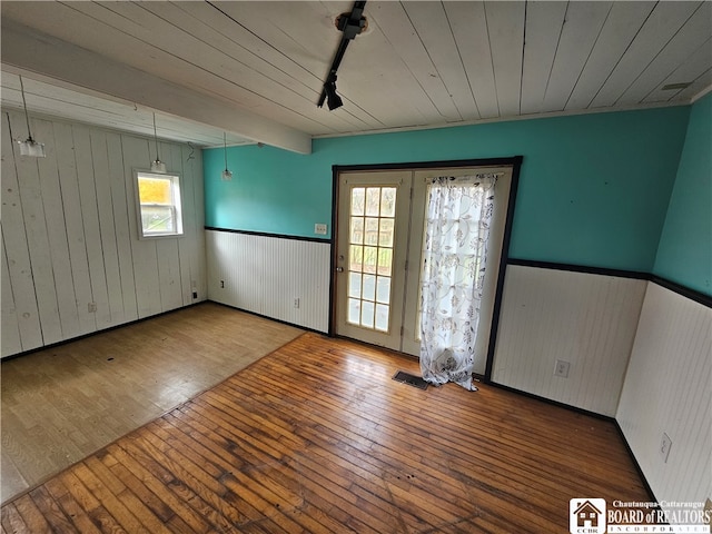 empty room with wood walls, hardwood / wood-style flooring, and track lighting