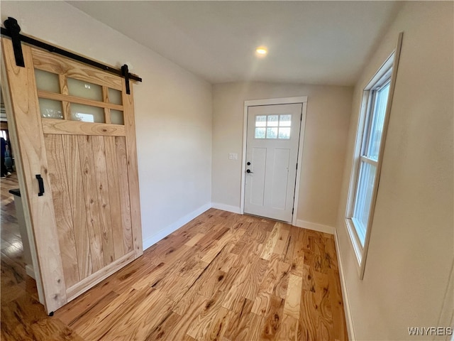 entrance foyer with light hardwood / wood-style floors, vaulted ceiling, and a barn door