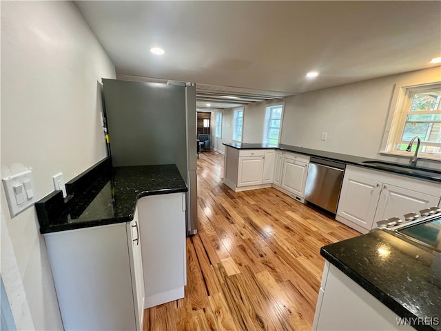 kitchen with dark stone countertops, sink, stainless steel dishwasher, white cabinetry, and light hardwood / wood-style floors