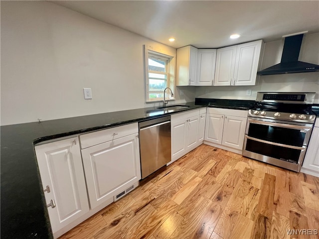 kitchen with white cabinetry, light hardwood / wood-style flooring, sink, wall chimney exhaust hood, and stainless steel appliances