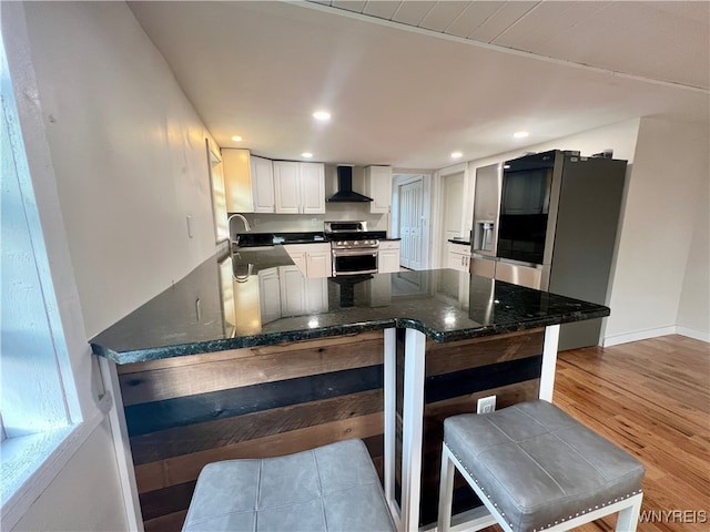 kitchen featuring appliances with stainless steel finishes, sink, white cabinetry, wall chimney exhaust hood, and light hardwood / wood-style flooring