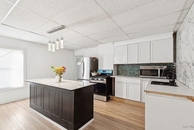 kitchen with white cabinets, hanging light fixtures, sink, light hardwood / wood-style floors, and stainless steel appliances