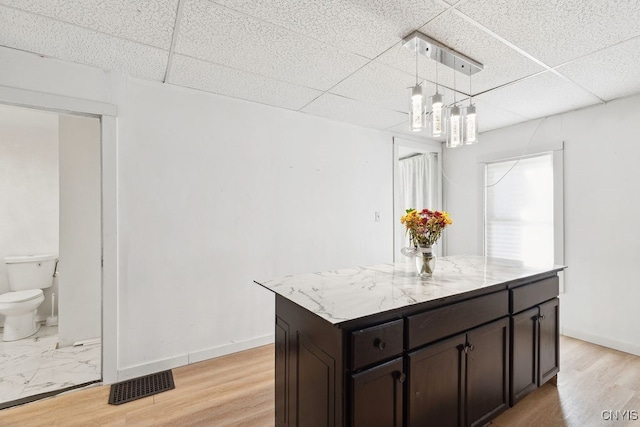 kitchen with light hardwood / wood-style floors, a center island, a paneled ceiling, and decorative light fixtures