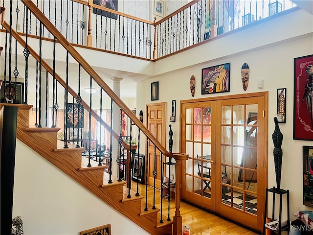 stairway featuring french doors, ornate columns, wood-type flooring, and a high ceiling