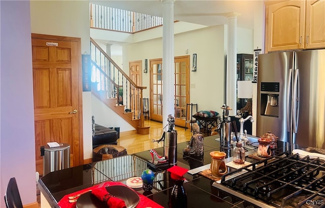 kitchen with light brown cabinetry, decorative columns, stainless steel fridge, a high ceiling, and hardwood / wood-style flooring