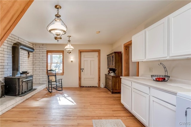 kitchen featuring light wood-style floors, light countertops, a wood stove, and white cabinetry