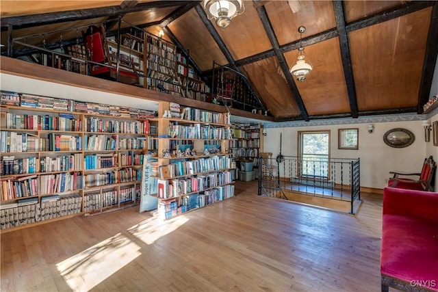 unfurnished room with high vaulted ceiling, beamed ceiling, wall of books, and wood finished floors