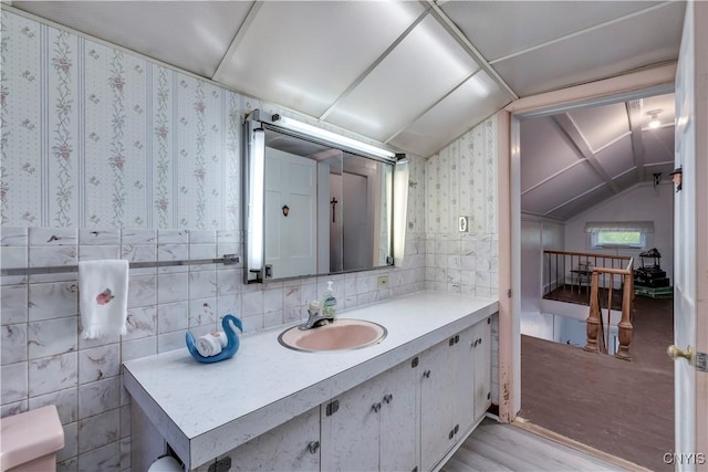 bathroom with tile walls, lofted ceiling, vanity, wood finished floors, and wallpapered walls