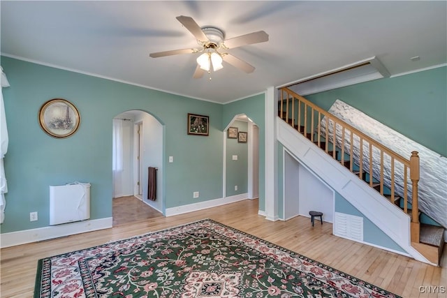 living area with arched walkways, crown molding, stairway, ceiling fan, and wood finished floors