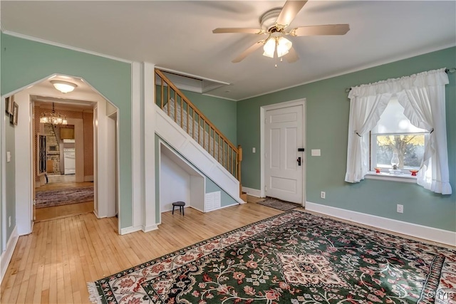 foyer featuring arched walkways, light wood-style flooring, stairway, ornamental molding, and baseboards