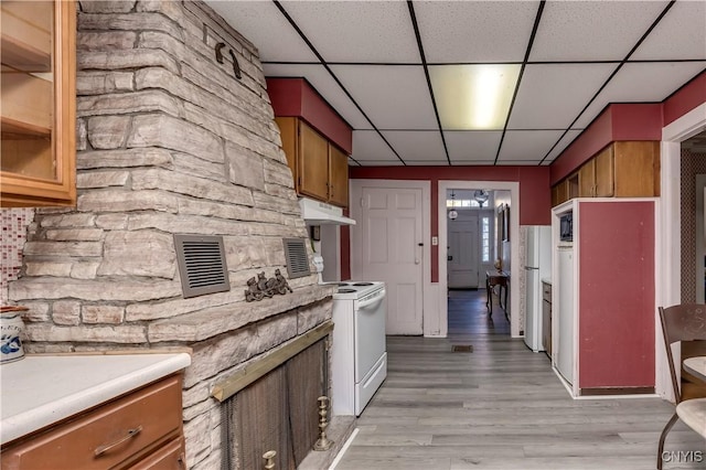 kitchen featuring under cabinet range hood, white appliances, visible vents, light countertops, and brown cabinets