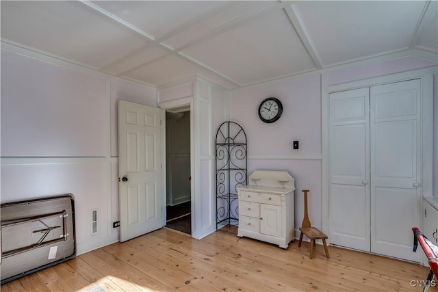 bedroom with a decorative wall, coffered ceiling, visible vents, light wood-style floors, and a closet