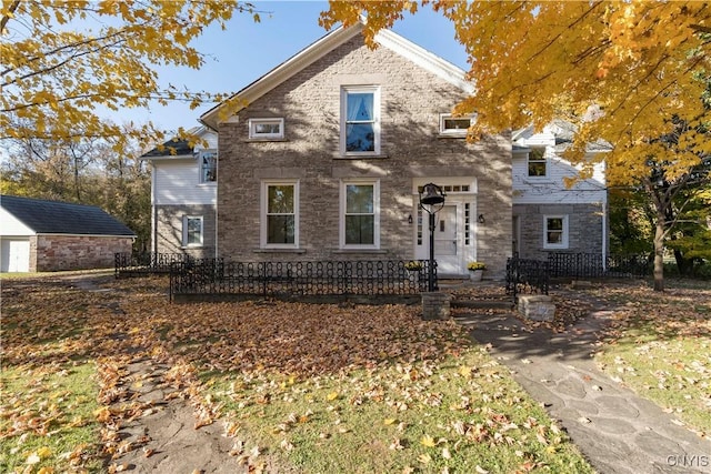 traditional home featuring stone siding, an outdoor structure, and fence