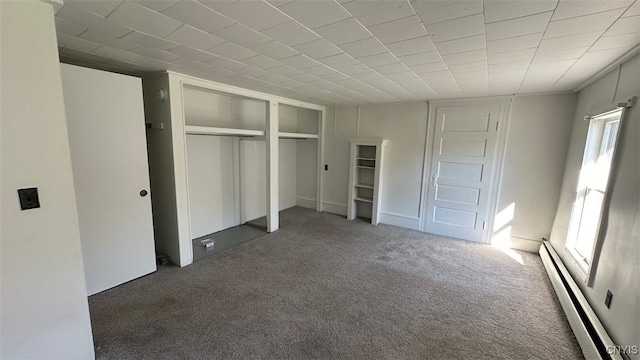 unfurnished bedroom featuring baseboard heating, dark carpet, and a closet