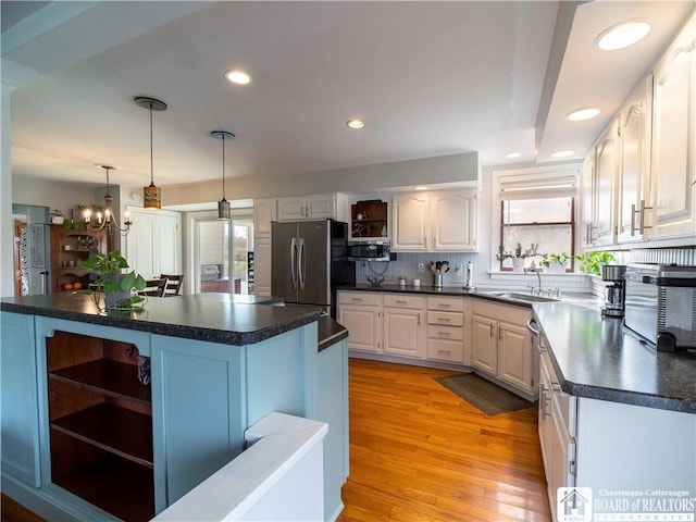 kitchen featuring sink, white cabinetry, stainless steel appliances, decorative light fixtures, and light wood-type flooring