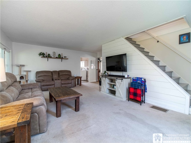 living room with washer / dryer, light carpet, and a textured ceiling