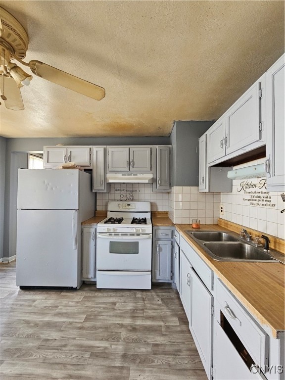 kitchen with white appliances, tasteful backsplash, sink, a textured ceiling, and light hardwood / wood-style flooring