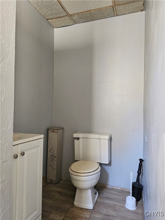 bathroom featuring vanity, a drop ceiling, wood-type flooring, and toilet