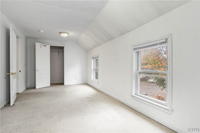 unfurnished bedroom with a closet, light carpet, a textured ceiling, and vaulted ceiling