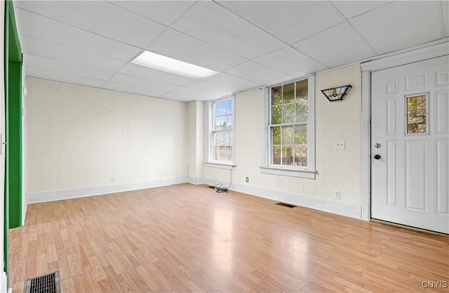 empty room featuring a drop ceiling, light hardwood / wood-style flooring, and wood walls