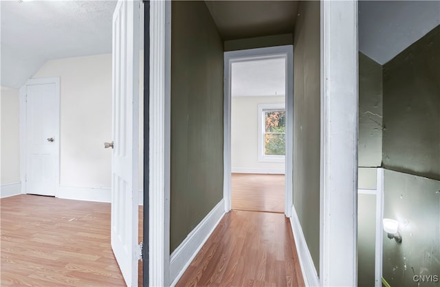 corridor with light wood-type flooring and vaulted ceiling