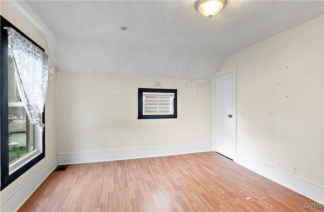 empty room featuring a wealth of natural light, lofted ceiling, hardwood / wood-style floors, and a textured ceiling