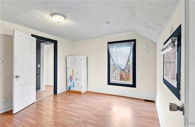 spare room with a textured ceiling, vaulted ceiling, and wood-type flooring