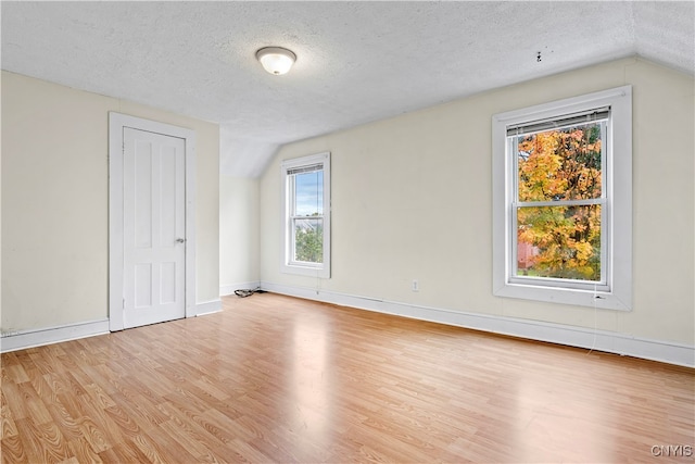 spare room featuring lofted ceiling, a textured ceiling, and light wood-type flooring